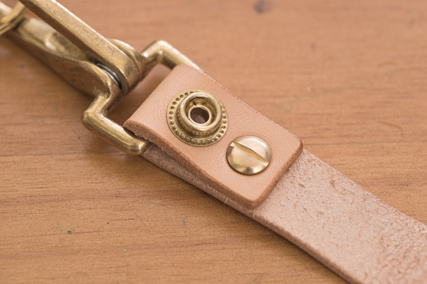 A natural leather key holder with a solid brass hardware and snap, close up of snap button and screw.
