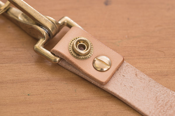 A natural leather key holder with a solid brass hardware and snap, close up of snap button and screw.