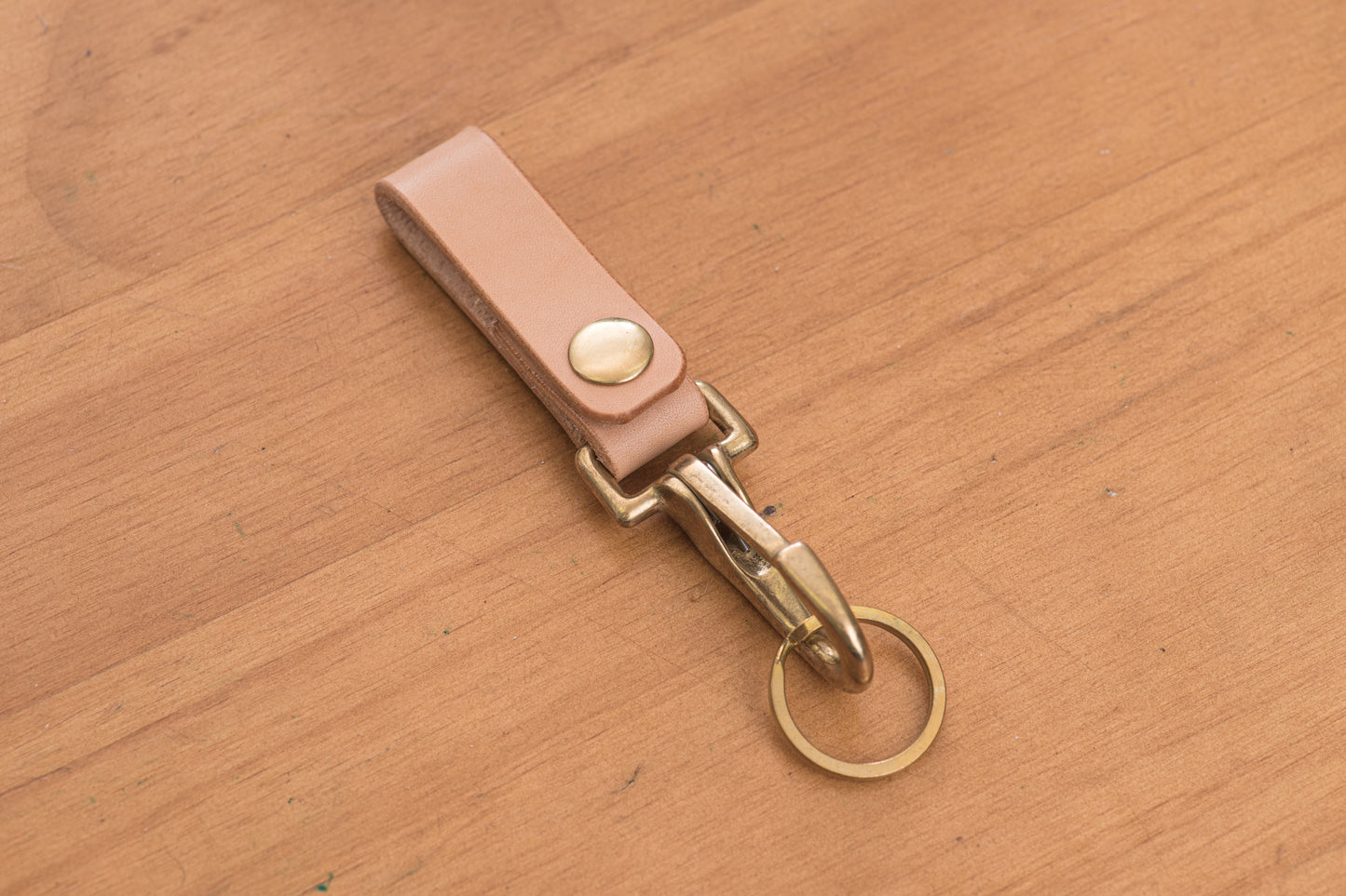 A natural leather key holder with a solid brass hardware and snap, displayed on a wooden surface.