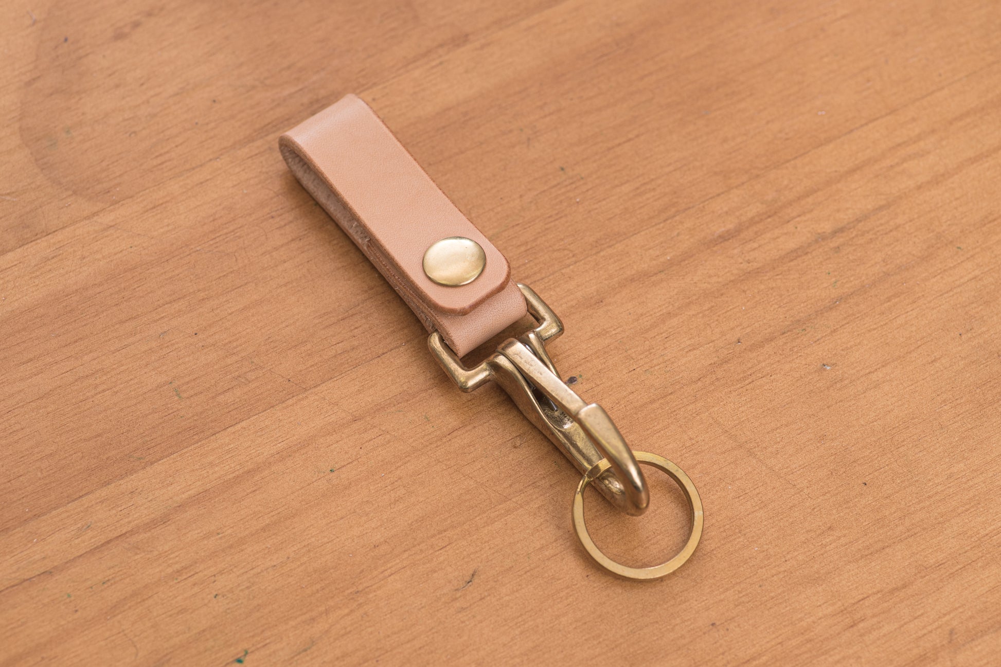 A natural leather key holder with a solid brass hardware and snap, displayed on a wooden surface.