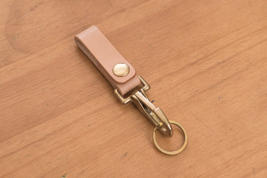 A natural leather key holder with a solid brass hardware and snap, displayed on a wooden surface.
