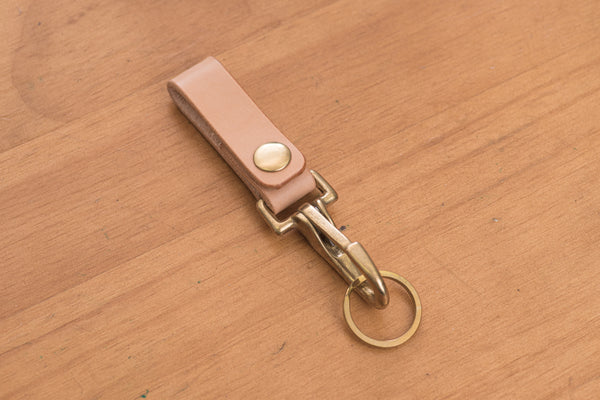 A natural leather key holder with a solid brass hardware and snap, displayed on a wooden surface.