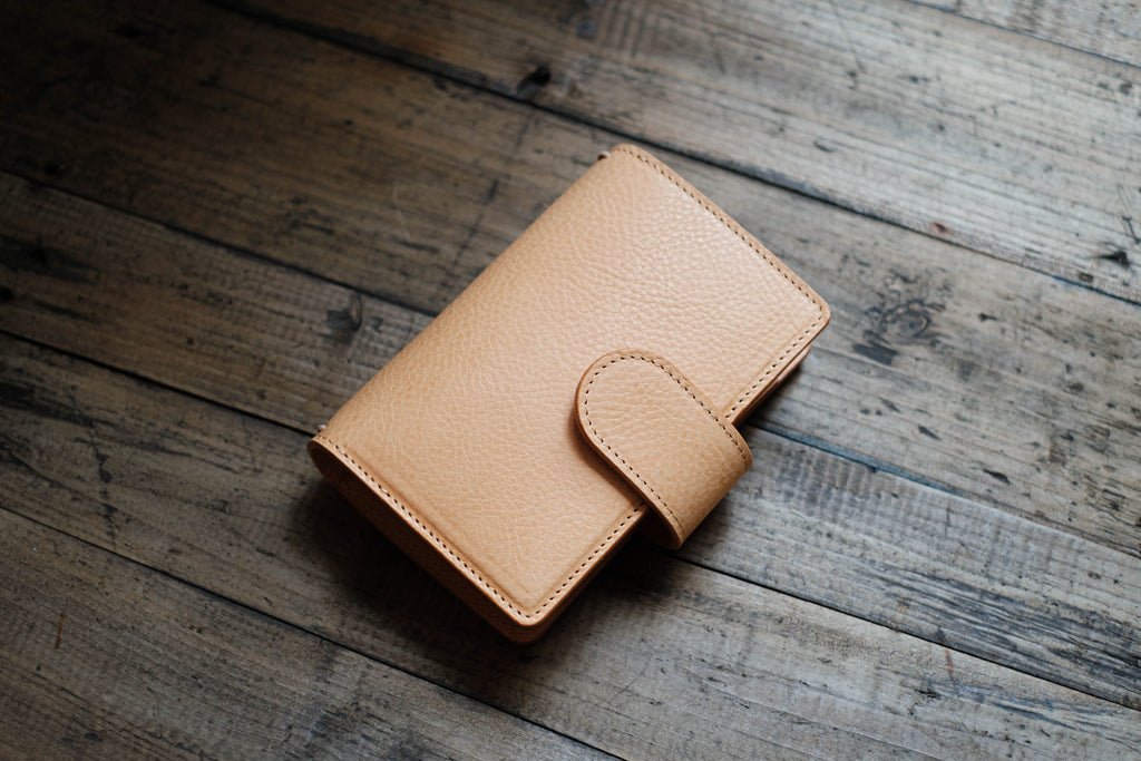 A natural lined traveler's notebook with card slots and a leather strap, displayed close