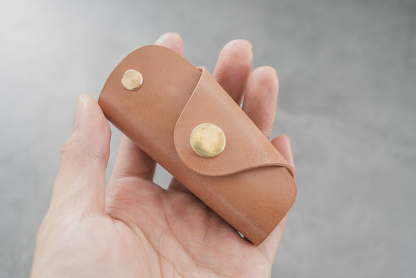 A natural Shell Cordovan leather key case with brass hardware and a removable brass wire hook.