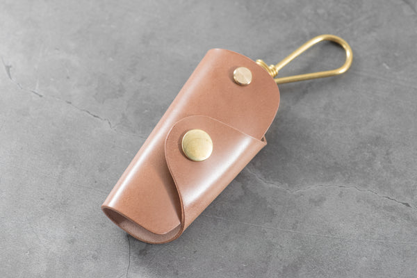A natural Shell Cordovan leather key case with brass hardware and a removable brass wire hook.