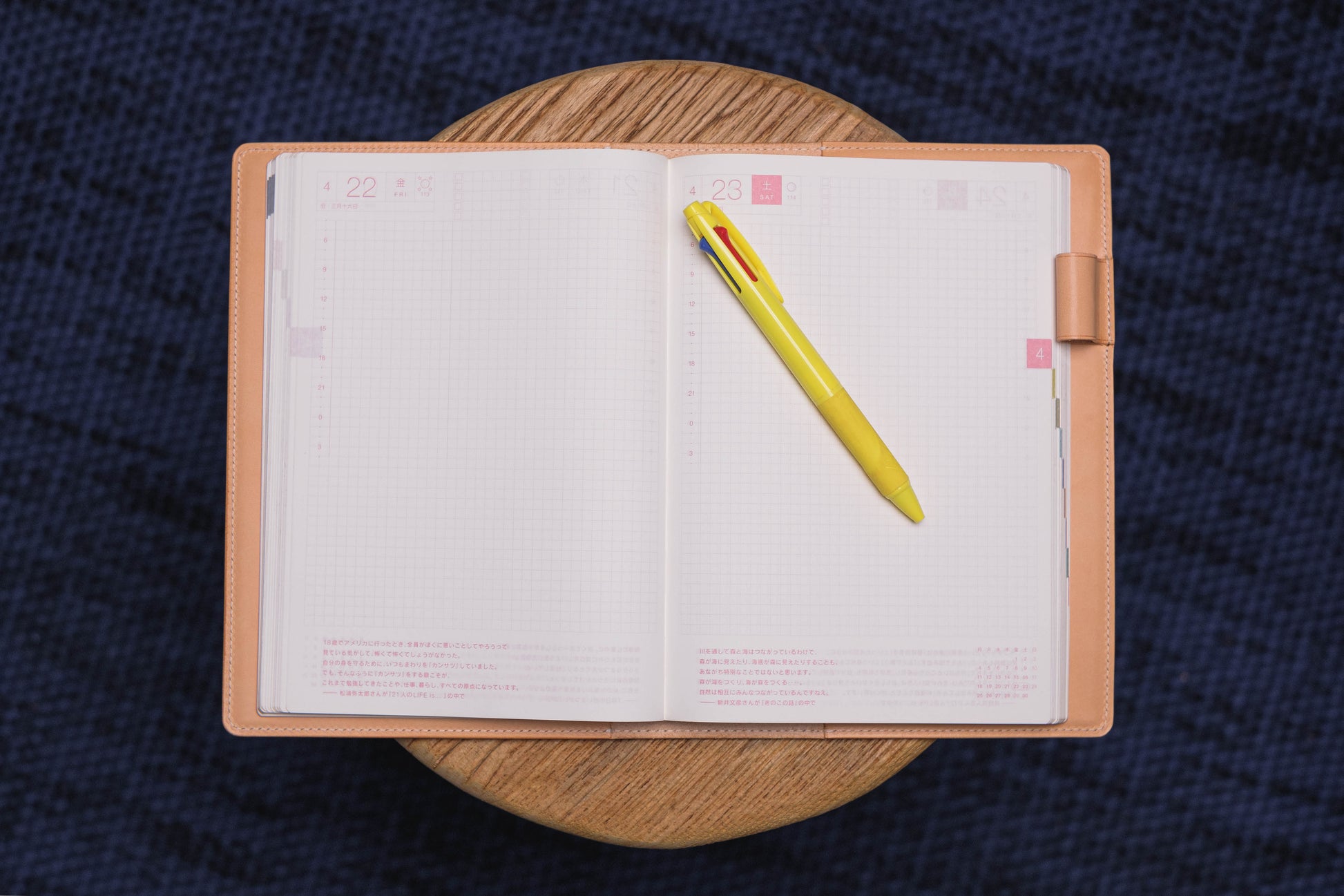 An open planner with a yellow pen on the right page. The planner has a natural leather cover and the pages are gridded. 