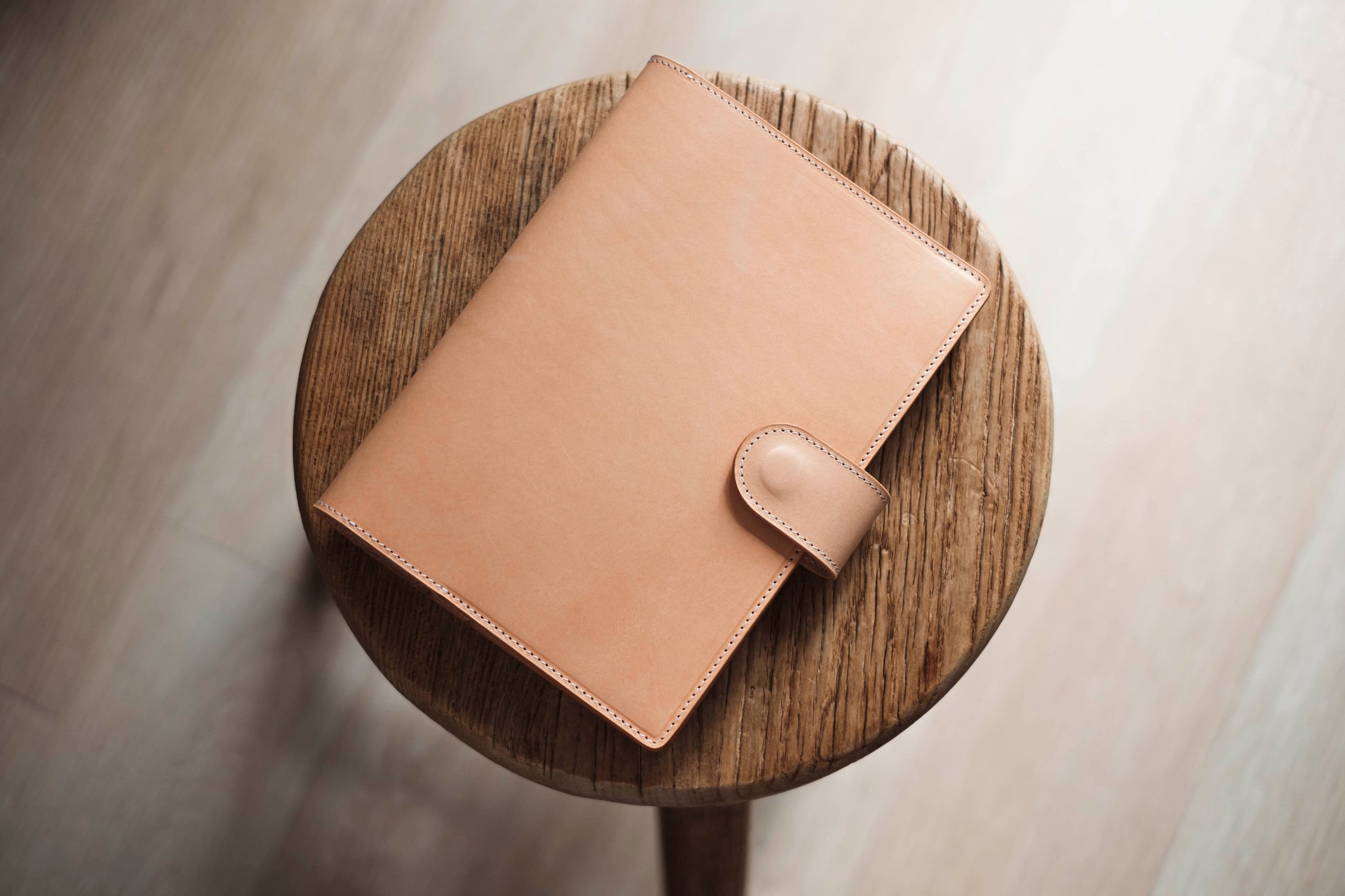 A natural leather notebook cover with a flap closure and a stitched edge. 