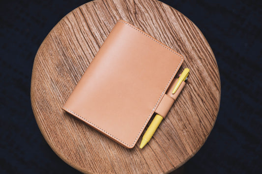 A natural leather notebook with a yellow pen tucked into the pen loop.