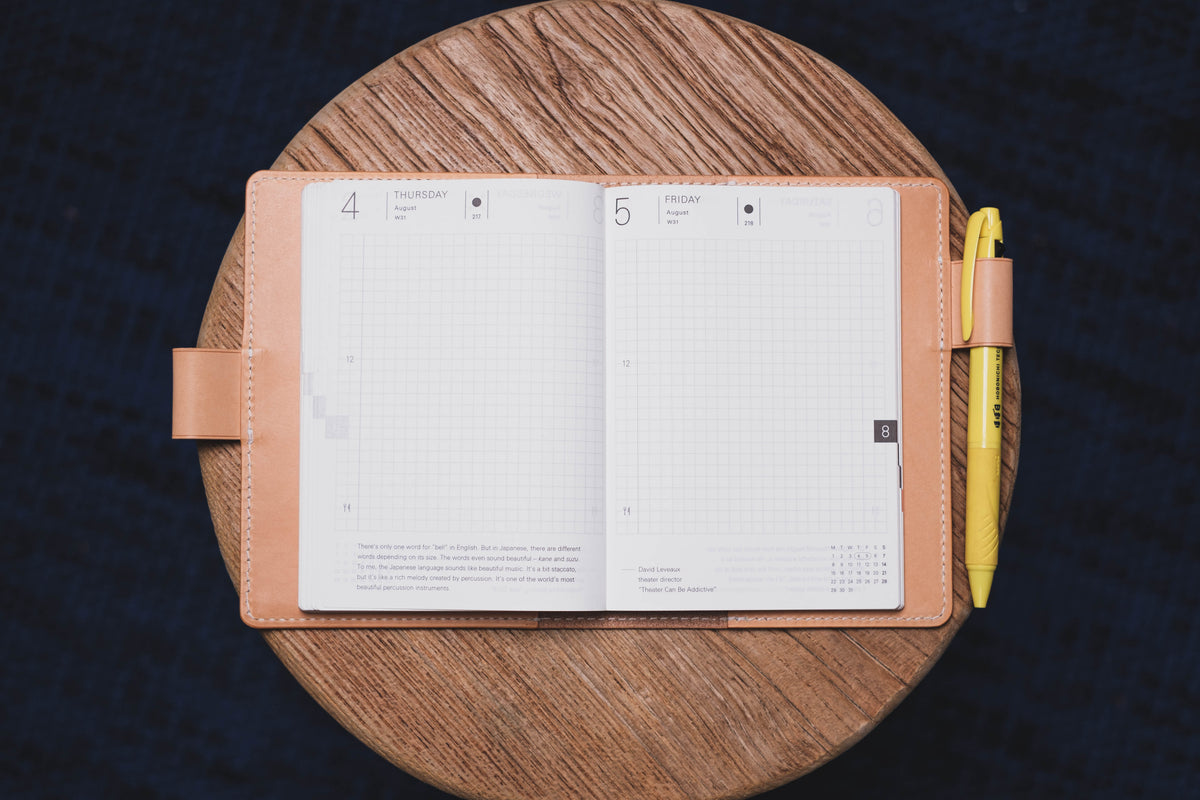 A natural leather notebook cover with a planner with a yellow pen. The planner is open to August 4th and 5th, with the days "Thursday" and "Friday" printed at the top of each page. 