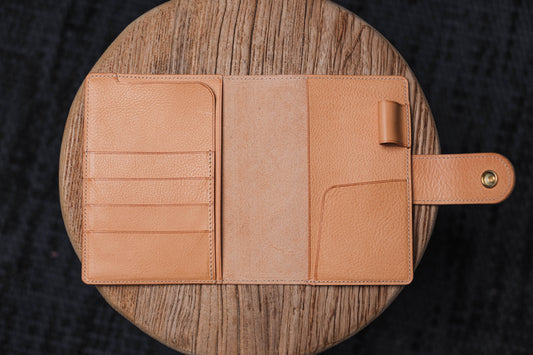 A natural pebbled leather notebook cover with card slots, pen loop, and snap closure.