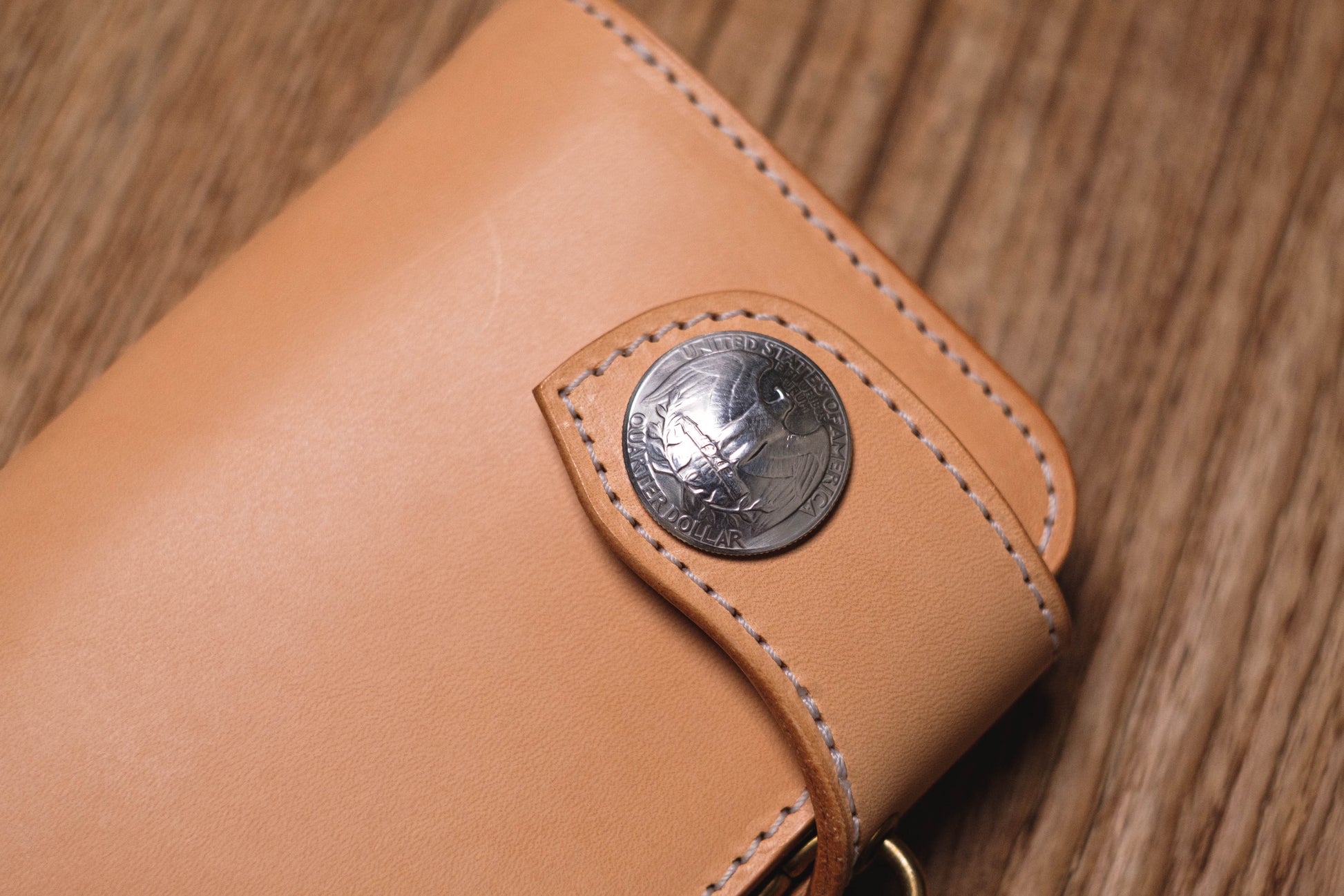 A natural leather wallet with a silver coin-shaped closure featuring the words "United States of America" and "One Dollar".