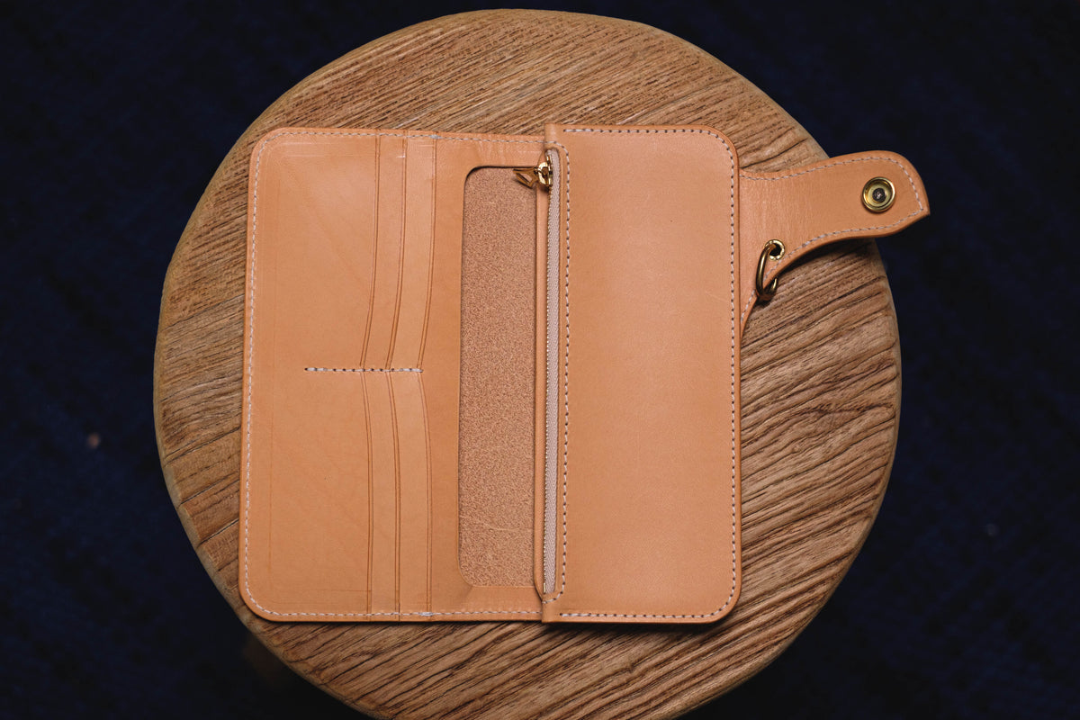 A natural leather wallet with a zippered compartment and a small leather strap with a metal ring. The wallet is open and the interior is visible.
