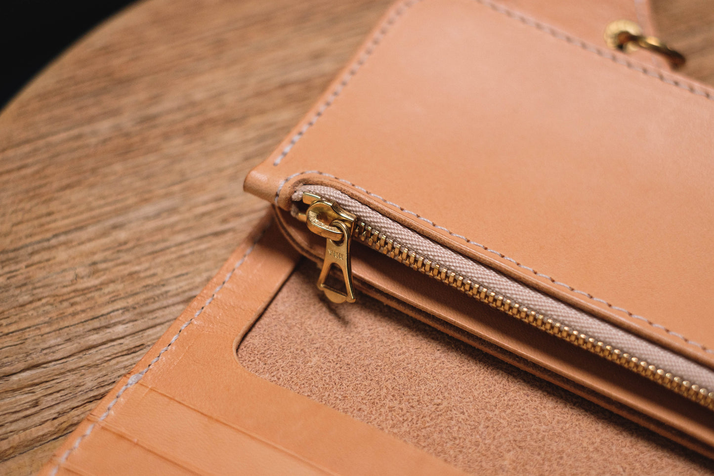 A natural leather wallet with a gold zipper. The zipper is partially open, revealing the inside of the wallet.