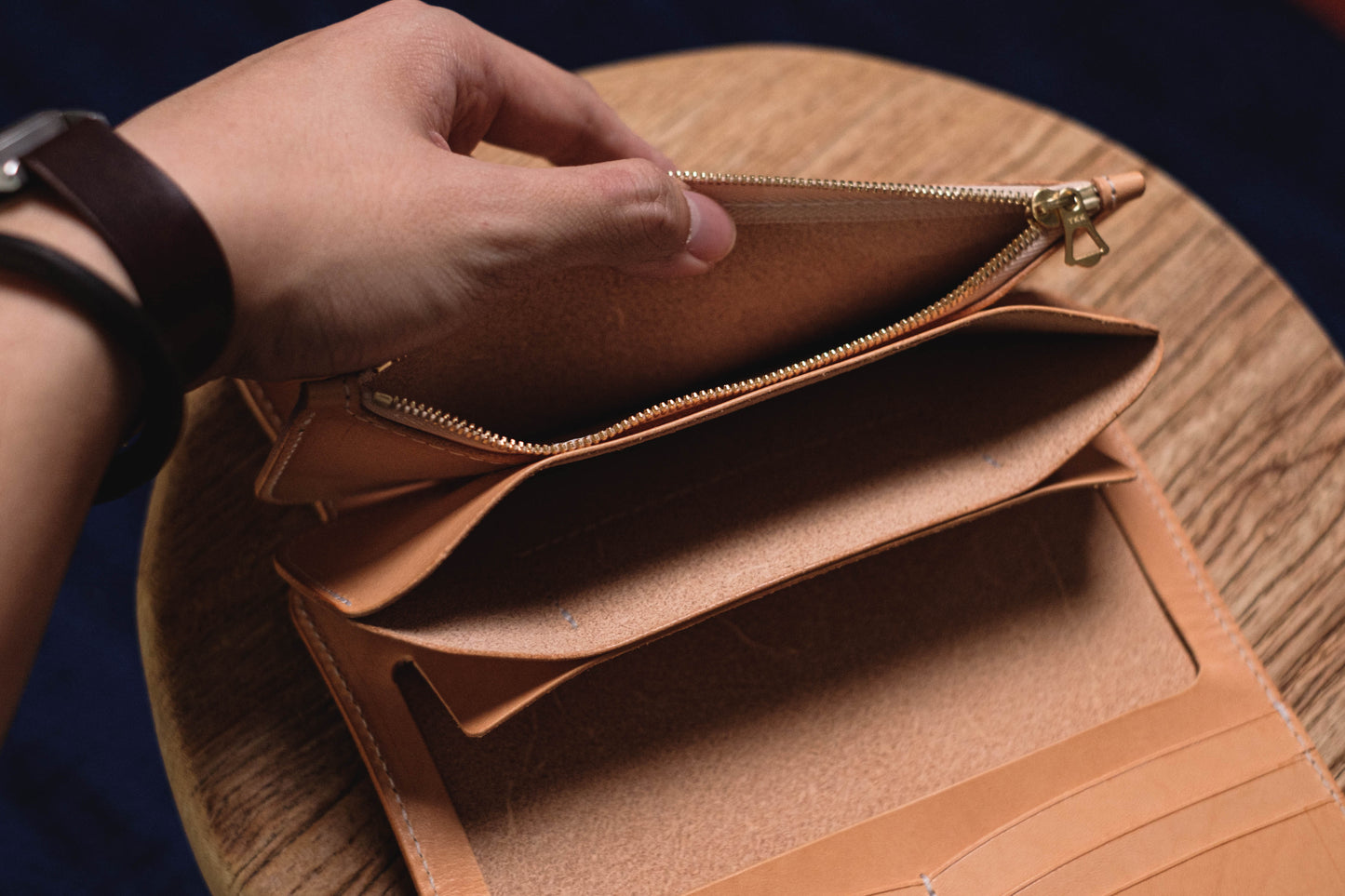 A natural leather wallet with a zipper closure and multiple compartments. The wallet is open and the interior is visible.