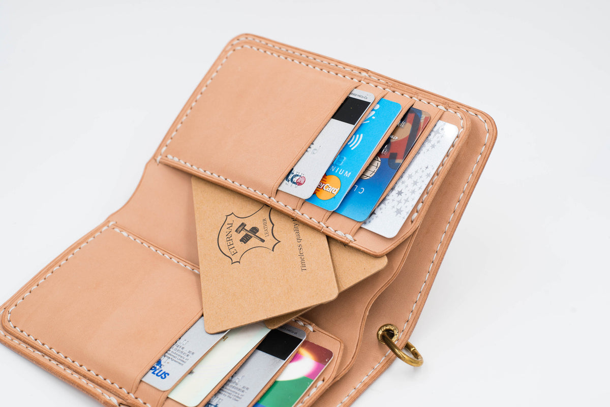 A natural leather wallet with multiple card slots and a flap closure. The wallet is open and filled with credit cards and a business card. The wallet has a stitched design and a metal ring.