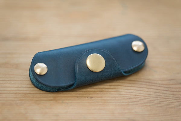 A navy blue leather key holder with brass snaps and screws.