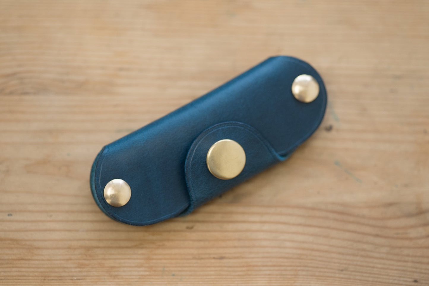 A navy blue leather key holder with brass snaps and screws.