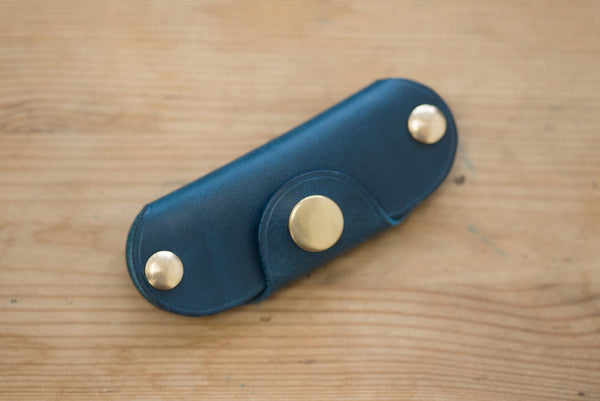 A navy blue leather key holder with brass snaps and screws.