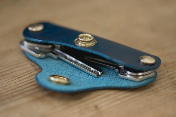 Navy blue leather key holder with brass snaps and screws, side view with keys