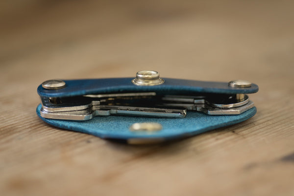 Navy blue leather key holder with brass snaps and screws, side view with keys