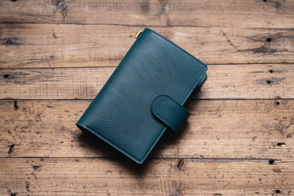 A navy blue leather traveler's notebook with card slots and a snap button closure, displayed closed