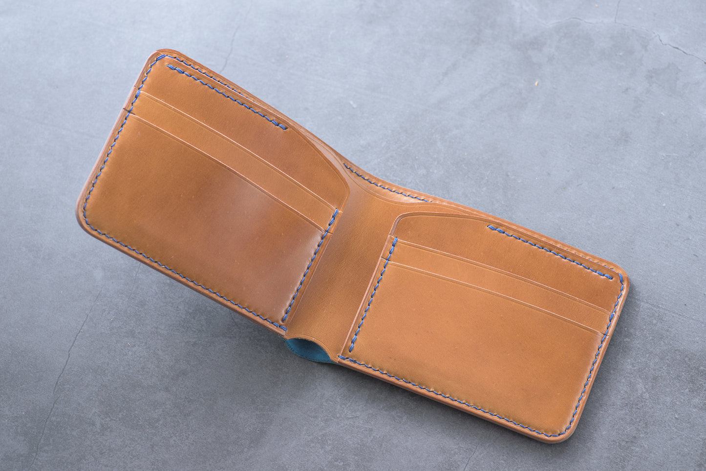 A whisky leather wallet with blue stitching, open to reveal multiple card slots and a billfold.