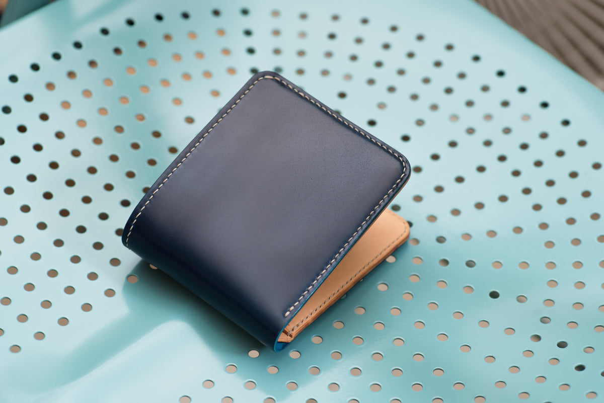 A two-tone billfold wallet with navy blue shell cordovan exterior and natural leather interior