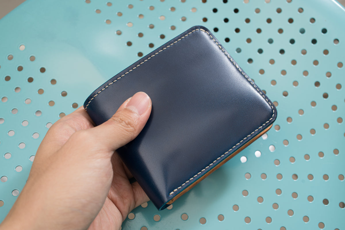 A two-tone billfold wallet with navy blue shell cordovan exterior and natural leather interior