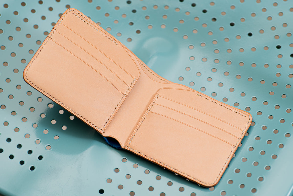 A natural bifold wallet featuring a smooth, natural finish with visible stitching along the edges. The interior displays two vertical card slots on each side, providing a clean, organized layout for holding cards and currency securely.