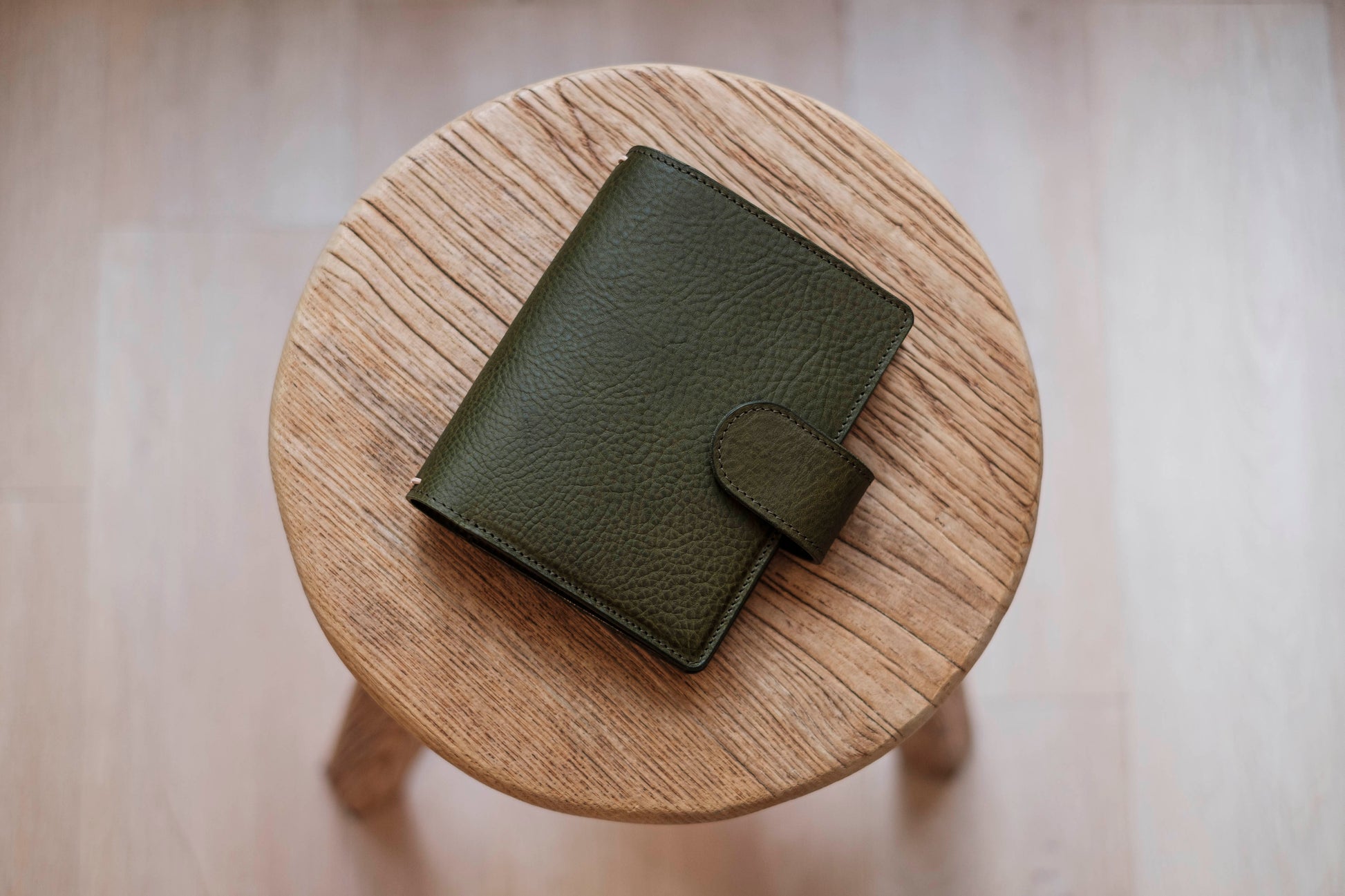 A olive green lined traveler's notebook with card slots and a leather strap, displayed close