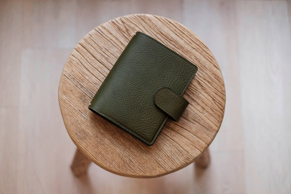 A olive green lined traveler's notebook with card slots and a leather strap, displayed close