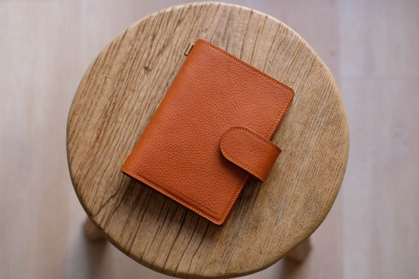 A orange brown lined traveler's notebook with card slots and a leather strap, displayed close