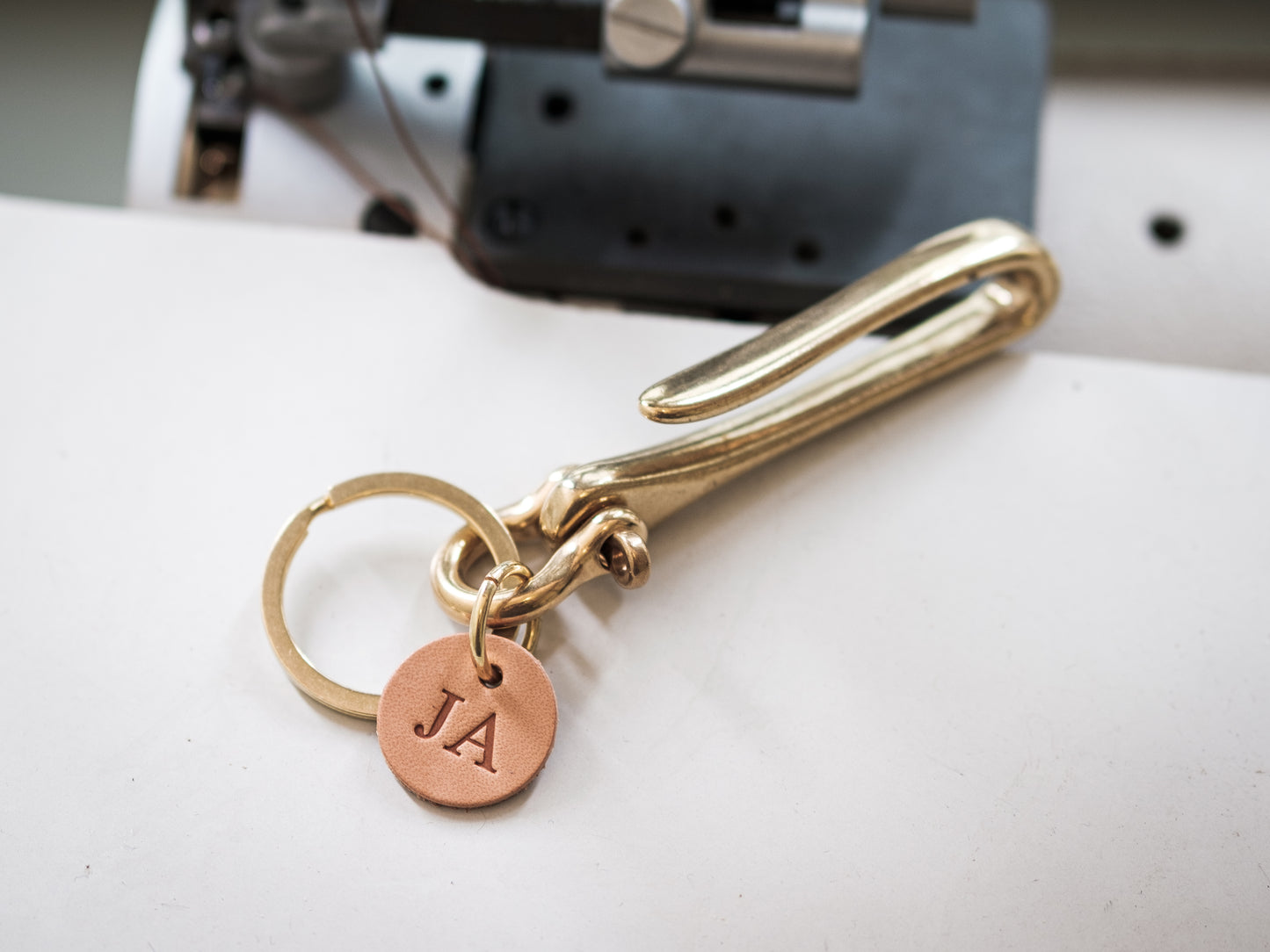 A gold-colored brass fish hook key holder with a leather tag and solid brass key ring with monogram on it.