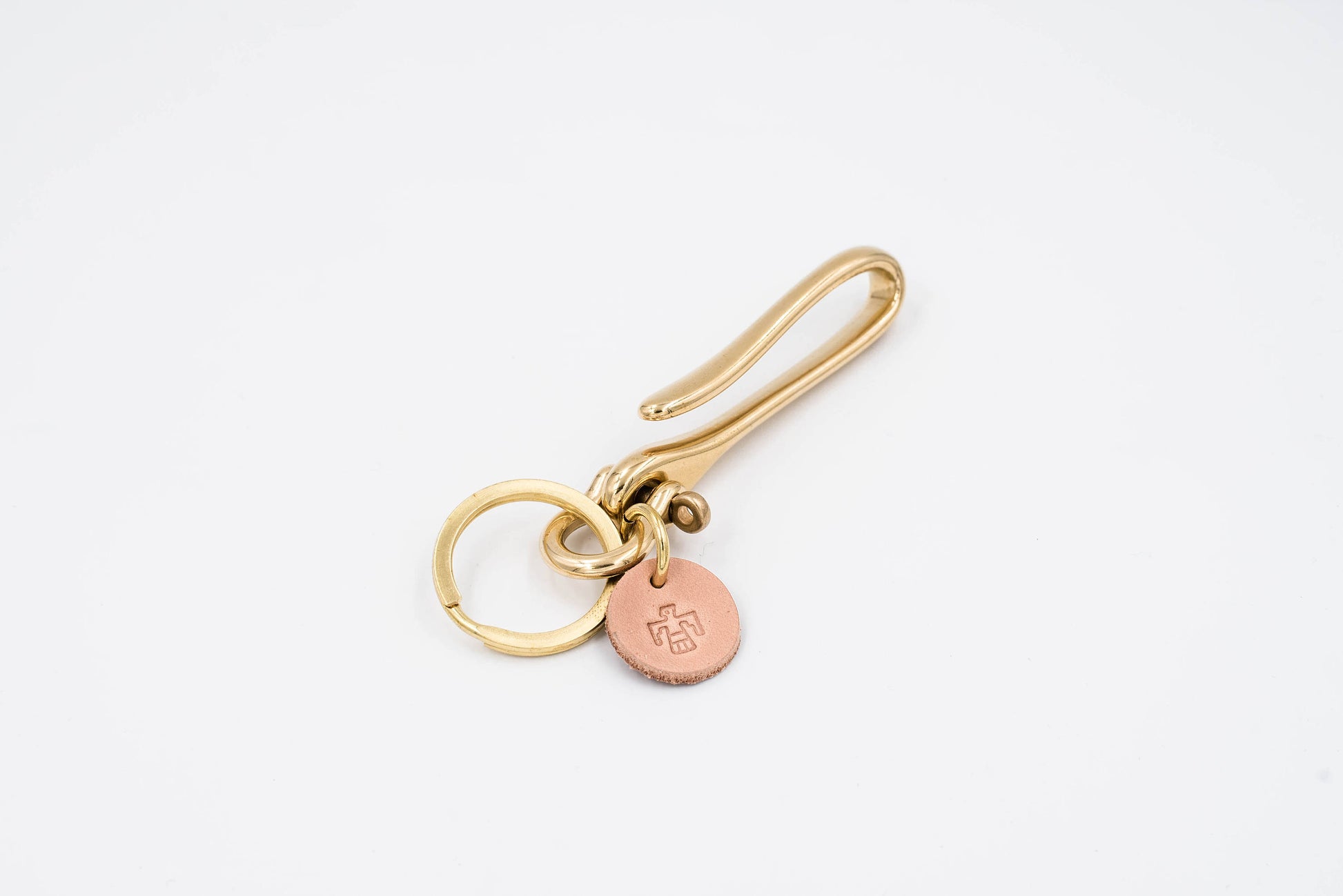 A gold-colored brass fish hook key holder with a leather tag and solid brass key ring.