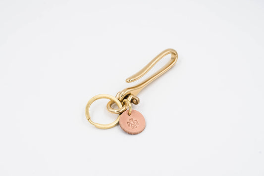 A gold-colored brass fish hook key holder with a leather tag and solid brass key ring.