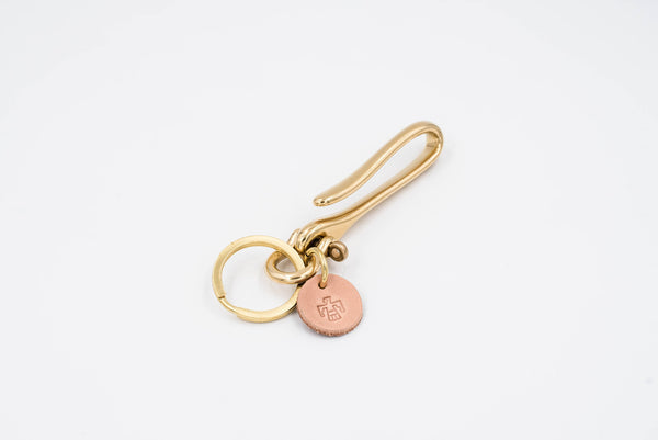 A gold-colored brass fish hook key holder with a leather tag and solid brass key ring.