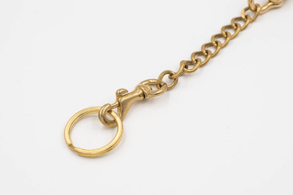 A polished brass fish hook with a solid brass chain attached to a key ring, designed to be hooked to a belt or belt loop, close up of key ring