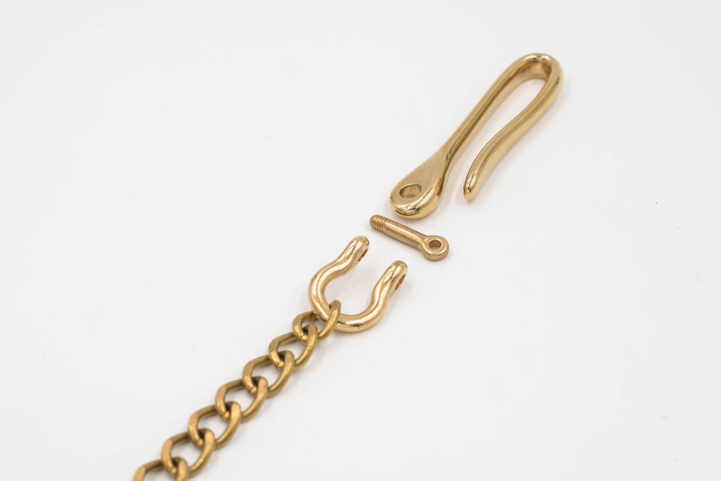 A polished brass fish hook with a solid brass chain attached to a key ring, designed to be hooked to a belt or belt loop, close up of fish hook