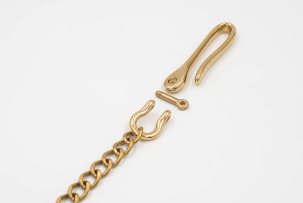 A polished brass fish hook with a solid brass chain attached to a key ring, designed to be hooked to a belt or belt loop, close up of fish hook