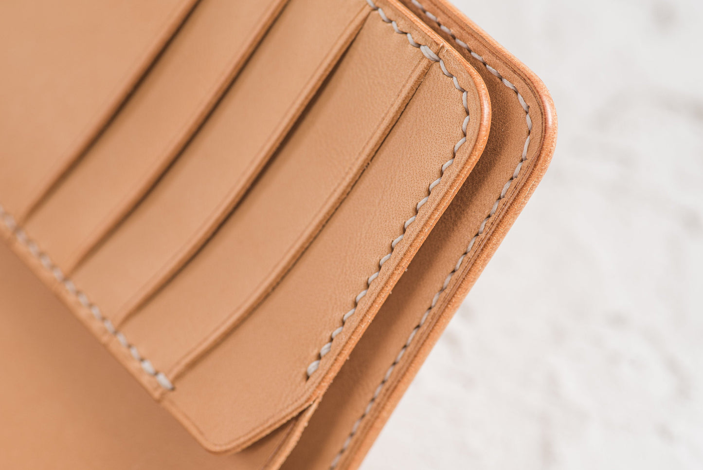 Close-up of a tan leather wallet with multiple card slots. The edges are neatly stitched with white thread, showcasing the craftsmanship. The wallet appears to be new and unused, with a clean, minimalist design.