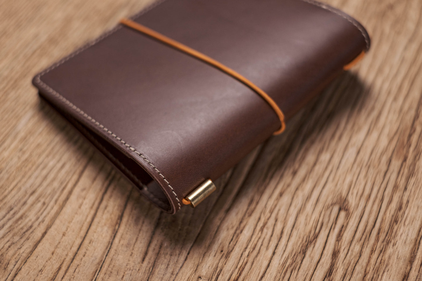 A brown Stitched Buttero Leather Traveler's Notebook and a elastic enclouse, Close up of elastic enclouse and stitching