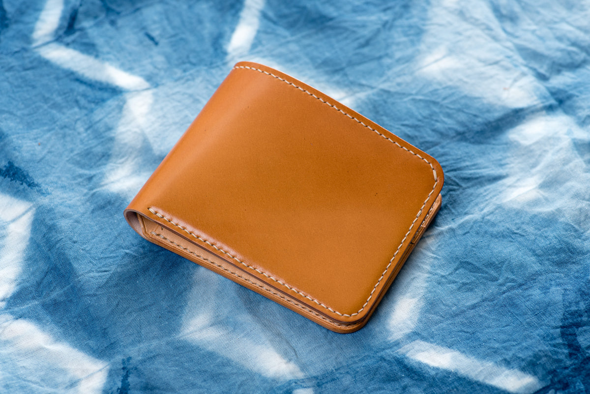 A whiskey bi-fold shell cordovan and natural leather billfold wallet with visible stitching and a subtle natural color leather interior